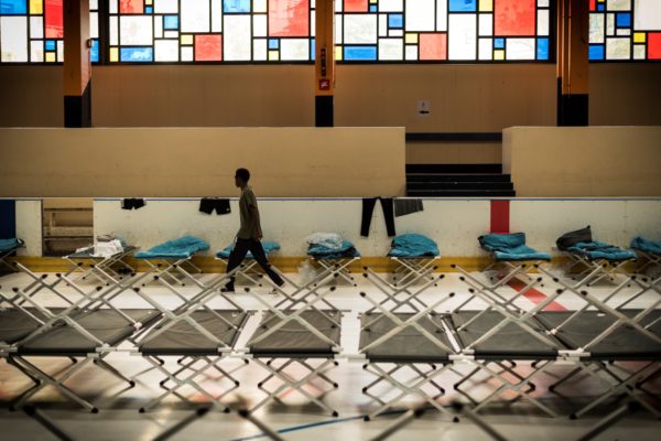 A migrant walk past camp beds in a former skating rink used as a pre-admission center for migrants in Cergy, outside Paris, on October 12, 2017, where migrants will be advised on the basis of their right to remain in France. 
Fifty people arrived this morning at the facility with a capacity of 200 beds maximum, the prefect of Val d'Oise, Jean-Yves Latournerie, said at a press conference. / AFP PHOTO / Lionel BONAVENTURE